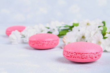 Pembe ve mor macaroons pembe ve beyaz çiçekler tarafından çevrili gri bir tablo.