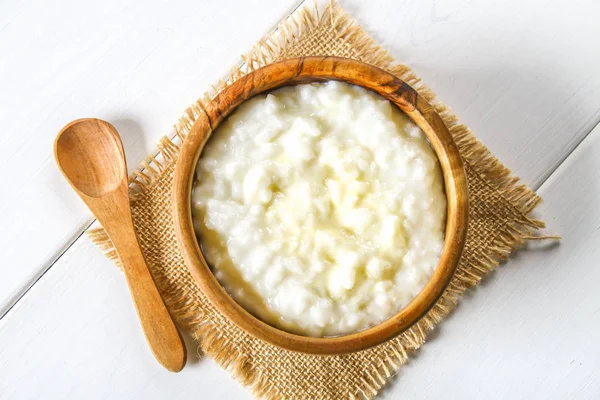 Χυλός από ρύζι γάλα με καρύδια και σταφίδες σε ξύλινες κύπελλα σε ένα λευκό ξύλινο τραπέζι. — Φωτογραφία Αρχείου