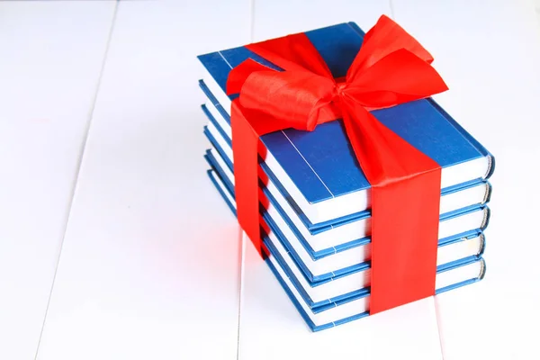 Een stapel boeken gebonden met een rood lint op een witte houten tafel. Een gift op de achtergrond van een schoolbord. — Stockfoto