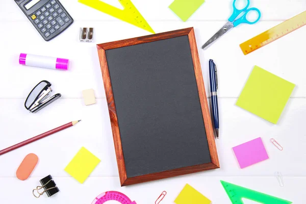 Schoolbord omgeven door briefpapier op een witte houten tafel. Kopiëren van de ruimte. — Stockfoto