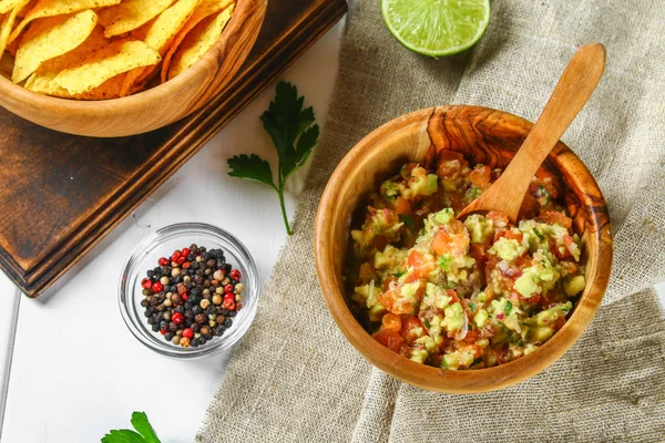 Guacomole is een traditionele Mexicaanse saus uit geraspte avocado, limoensap, rode ui, tomaten, knoflook en chili. Geserveerd met nachos chips. — Stockfoto