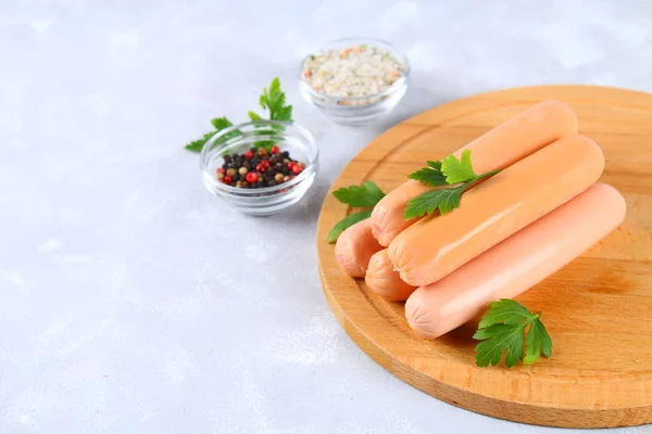 Bir gri beton masada ahşap bir gemide çiğ sosis.