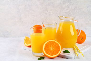 Cam bardak ve bir sürahi taze portakal suyu üzerine gri masa lambası turuncu ve sarı renkli boruları dilimleri ile.