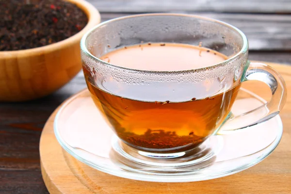 Thé noir chaud dans une tasse en verre et thé sec sur une table en bois . — Photo