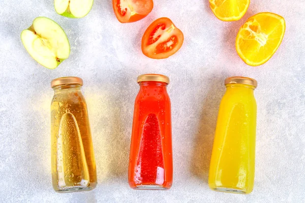 Bottles with fresh orange, apple, tomato juice on a gray concrete table. Fruits and vegetables around. Top view. Flat Lay. — Stock Photo, Image