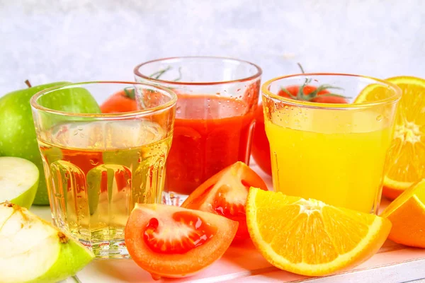 Bicchieri con arancia fresca, mela, succo di pomodoro su un tavolo di cemento grigio. Lobuli Frutta e verdura intorno . — Foto Stock