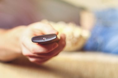 Bir adam bir kase patlamış mısır ve elinde bir uzaktan kumanda ile Tv kanepede görünüyor..