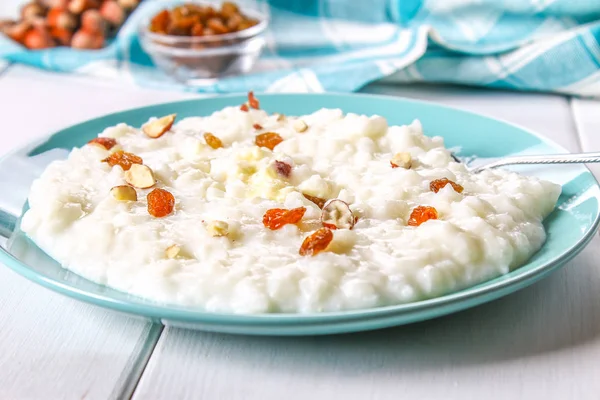 Porridge di latte di riso con noci e uva passa in un piatto blu su un tavolo di legno bianco . — Foto Stock