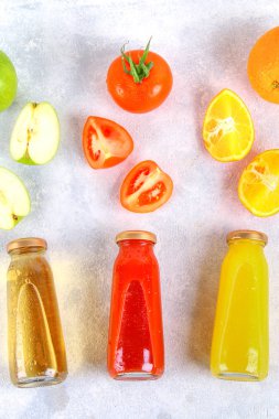 Şişe taze portakal, elma, domates suyu bir gri beton tablo. Meyve ve sebze çevresinde. Üstten Görünüm. Düz Lay.