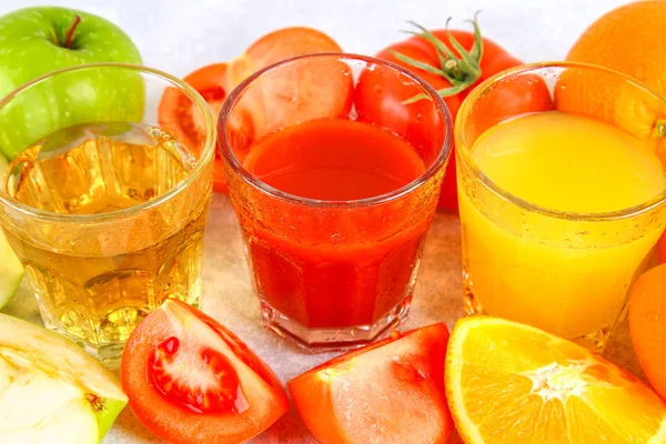 Vasos con naranja fresca, manzana, jugo de tomate sobre una mesa de hormigón gris. Lobulillos Frutas y verduras alrededor . — Foto de Stock