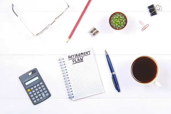 Bloc-notes avec le texte : plan de retraite. Table blanche avec calculatrice, cactus, papier à lettres, tasse à café, stylo, lunettes . — Photo