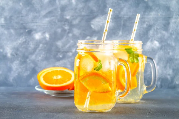 Orange detox water in mason jars on a gray concrete background. Healthy food, drinks.