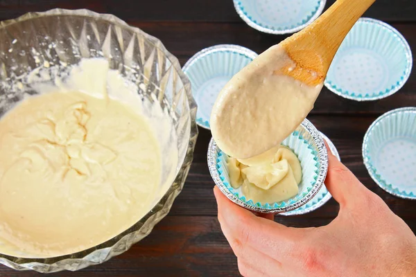 Mãos derramando massa em moldes para muffins em uma mesa de madeira . — Fotografia de Stock