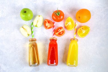 Şişe taze portakal, elma, domates suyu ve renkli tübüllerin bir gri beton tablo ile. Meyve ve sebze çevresinde. Üstten Görünüm. Düz Lay.