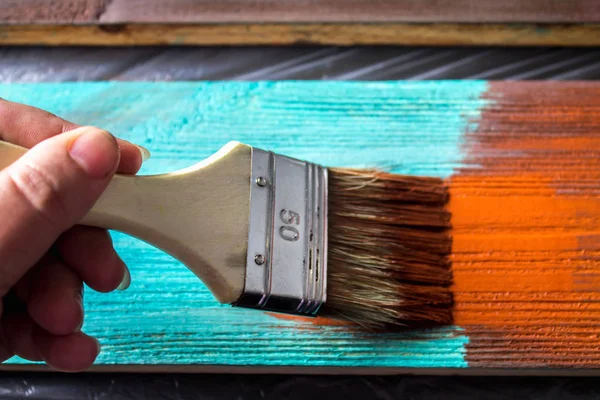 Escova com tinta na mão. Um homem pinta placas azuis em um pincel de tinta marrom . — Fotografia de Stock