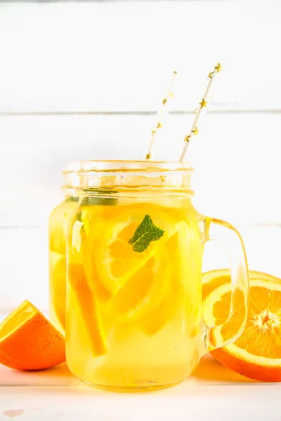 Agua de desintoxicación naranja en frascos de albañil sobre una mesa de madera blanca. Comida saludable, bebidas . —  Fotos de Stock