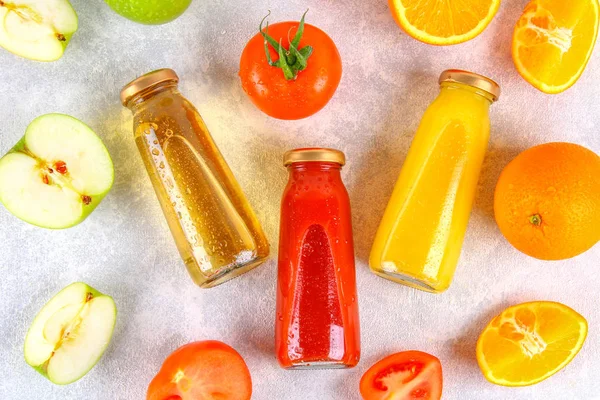 Botellas con naranja fresca, manzana, jugo de tomate sobre una mesa de hormigón gris. Frutas y verduras alrededor. Vista superior. Piso Lay . — Foto de Stock