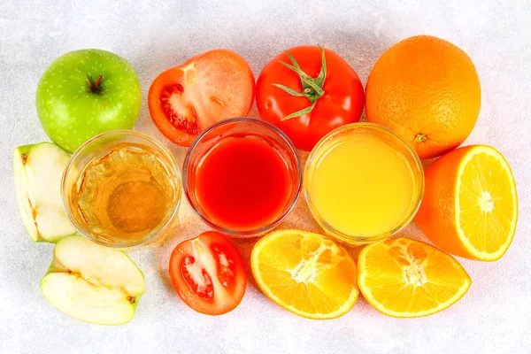 Vasos con naranja fresca, manzana, jugo de tomate sobre una mesa de hormigón gris. Lobulillos Frutas y verduras alrededor. Vista superior . — Foto de Stock