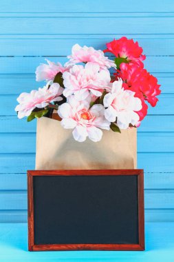 Pembe peonies mavi ahşap bir masa bir kara tahta ile bir zanaat paket. Kartpostal tatil için. Kopyalama alanı.