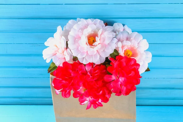 Peonías rosadas en un paquete de artesanía sobre una mesa de madera azul. Postal para las vacaciones . — Foto de Stock