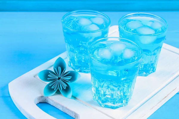 Cóctel azul con hielo y menta en vasos sobre una mesa de madera blanca sobre una mesa azul . — Foto de Stock