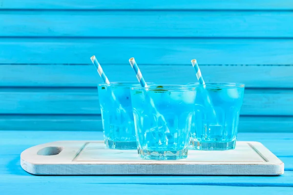 Cóctel azul con hielo y menta en vasos sobre una mesa de madera blanca sobre una mesa azul . — Foto de Stock
