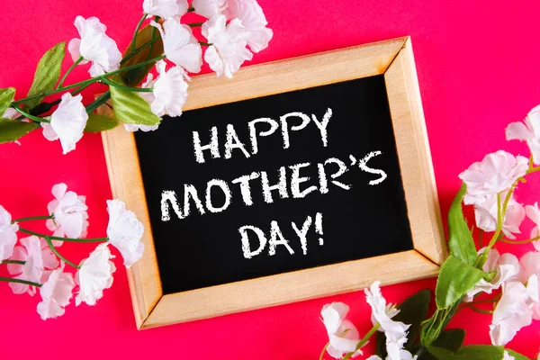 Chalkboard em uma moldura de madeira com uma caixa vazia cercada por flores brancas em um fundo rosa. Feliz dia da mãe . — Fotografia de Stock