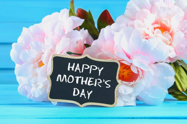 Peonías rosadas con una pizarra sobre una mesa de madera azul. Una postal para las vacaciones. Feliz día de la madre . — Foto de Stock