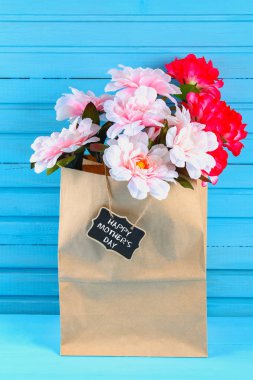 Pembe peonies mavi ahşap bir masa bir kara tahta ile bir zanaat paket. Kartpostal tatil için. Mutlu anneler günü