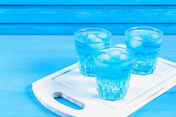 Cóctel azul con hielo y menta en vasos sobre una mesa de madera blanca sobre una mesa azul . — Foto de Stock