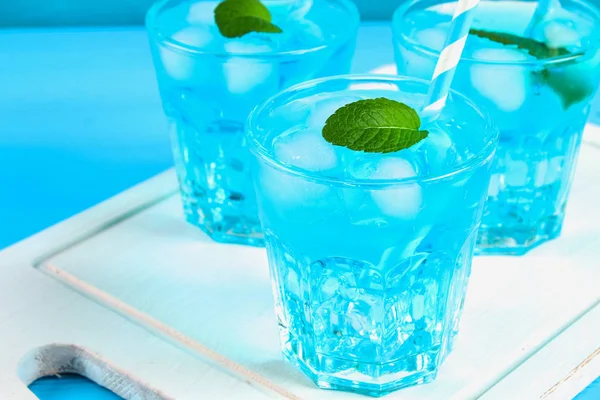 Blue cocktail with ice and mint in glasses on a white wooden board on a blue table. — Stock Photo, Image
