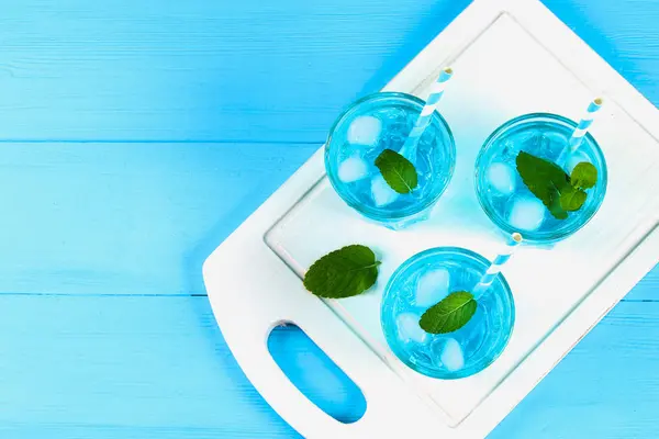 Cóctel azul con hielo y menta en vasos sobre una mesa de madera blanca sobre una mesa azul. Vista superior . — Foto de Stock