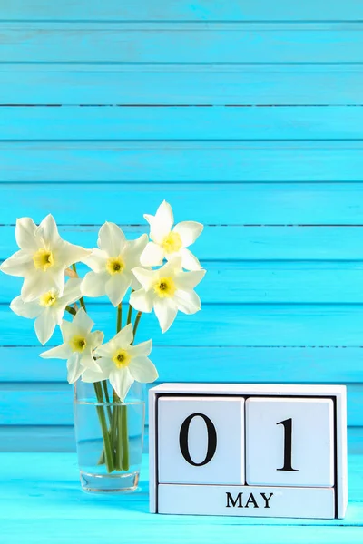 Calendário de madeira branco com o texto: 1 de maio. Flores brancas de narcisos em uma mesa de madeira azul. Dia do Trabalho e Primavera . — Fotografia de Stock