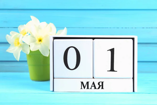 Calendario de madera blanca con el texto en ruso: 1 de mayo. Flores blancas de narcisos sobre una mesa de madera azul. Día del Trabajo y Primavera . — Foto de Stock