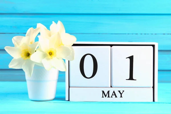 Białe drewniane kalendarz z tekstem: 1 maja. Białe kwiaty żonkile na niebieskim drewnianym stole. Święto pracy i wiosna. — Zdjęcie stockowe