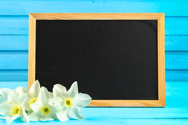 Narcissen bloemen en leeg schoolbord label op houten achtergrond, kopie ruimte. — Stockfoto