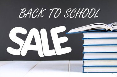 Bir kara tahta arka plan üzerinde kitap yığını. Yığının üstüne bir gizli kitap. Satılık.