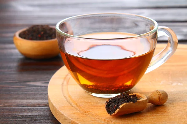 Thé noir chaud dans une tasse en verre et thé sec sur une table en bois . — Photo