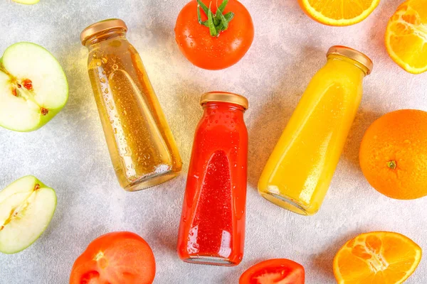 Botellas con naranja fresca, manzana, jugo de tomate sobre una mesa de hormigón gris. Frutas y verduras alrededor. Vista superior. Piso Lay . — Foto de Stock