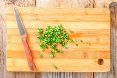 Erkek el kesme tahtası üzerinde eski bir ahşap masa üzerinde yeşil soğan kesmek.