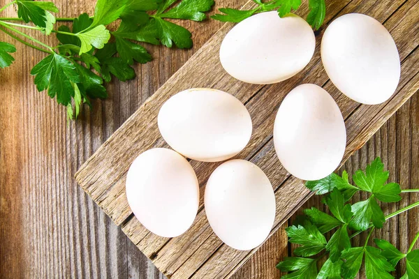 Свежие белые сырые куриные яйца с петрушкой на старом деревянном столе . — стоковое фото
