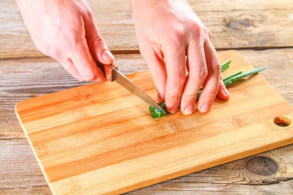 Męskie ręce zielone cebulę na pokładzie cięcia na starym drewnianym stole. — Zdjęcie stockowe