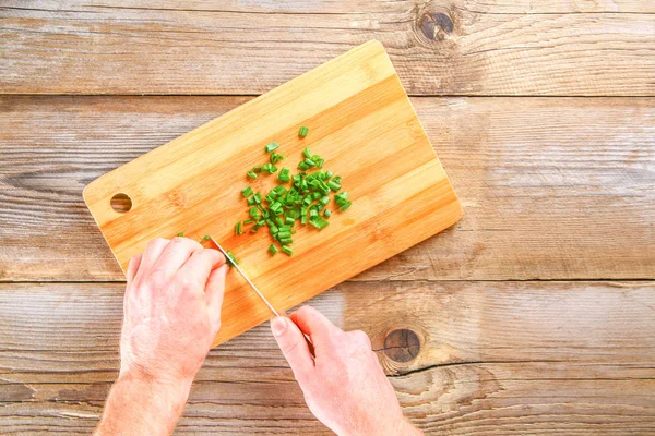 Male hands cut a green onion on a cutting board on an old wooden table. — Stock Photo, Image