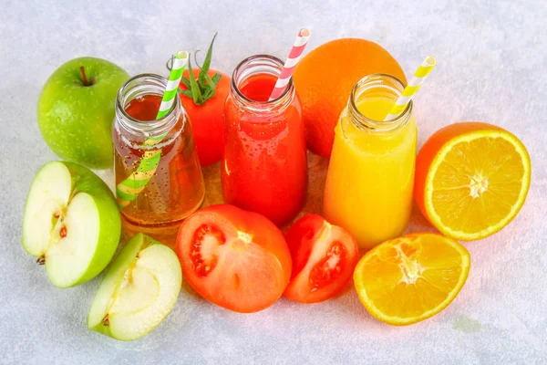 Bottles with fresh orange, apple, tomato juice and colored tubules on a gray concrete table. — Stock Photo, Image