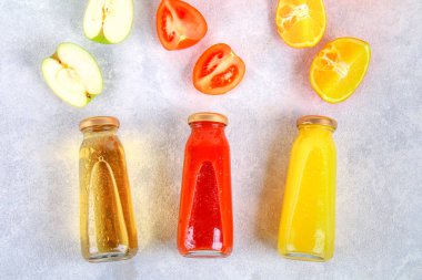 Şişe taze portakal, elma, domates suyu bir gri beton tablo. Meyve ve sebze çevresinde. Üstten Görünüm. Düz Lay.