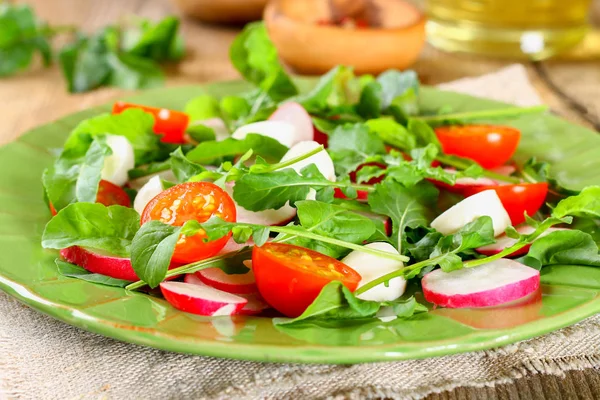 Vegetarian salad of arugula, tomato, radish and mozzarella cheese on an old wooden table. — Stock Photo, Image
