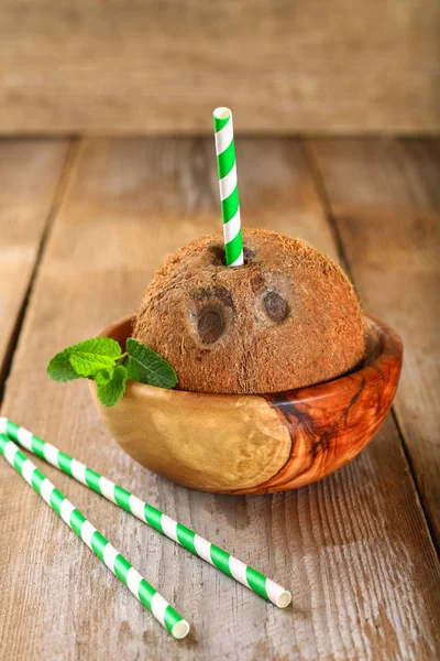 Coconut with juice inside, mint and green paper tubes on an old wooden table. — Stock Photo, Image