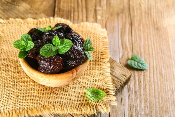 Ciruelas pasas con hojas de menta en un tazón sobre una mesa de madera vieja . — Foto de Stock