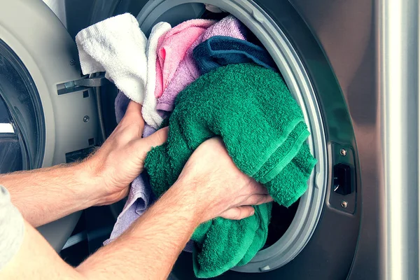 Man taking color clothes from washing machine. A drum of washing machine full of dirty laundry in bathroom.