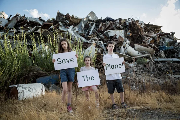 Save the planet. young kids holding signs standing in a huge junkyard — Stock Photo, Image